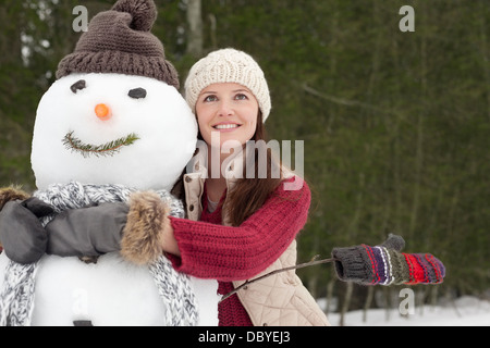 Glückliche Frau umarmt Schneemann in Wäldern Stockfoto