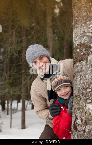 Porträt der glückliche Vater und Sohn hinter Baumstamm im verschneiten Wald Stockfoto