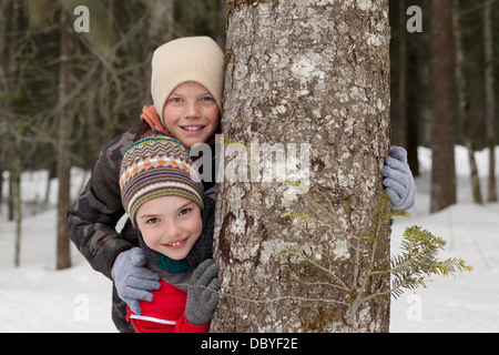 Porträt von glücklichen jungen hinter Baumstamm im verschneiten Wald Stockfoto