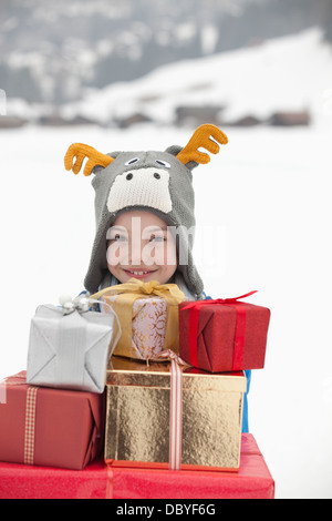 Porträt von lächelnden jungen Rentier Hut und Durchführung Stapel von Weihnachtsgeschenke im Schnee Stockfoto