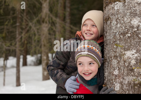 Happy Boys gelehnt Baumstamm im verschneiten Wald Stockfoto