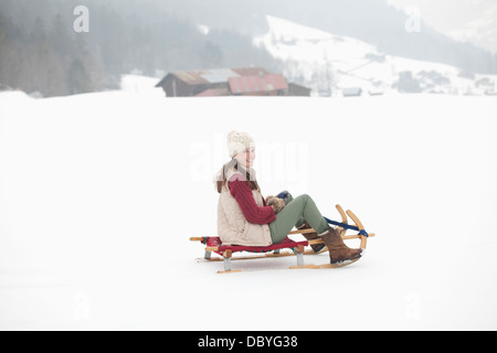 Porträt der lächelnde Frau Rodeln in schneebedecktes Feld Stockfoto