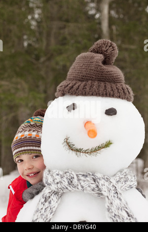 Porträt eines lächelnden jungen hinter Schneemann mit Zipfelmütze Stockfoto