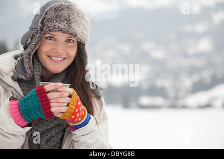 Porträt der glückliche Frau in Pelzmütze Kaffeetrinken in schneebedecktes Feld Stockfoto