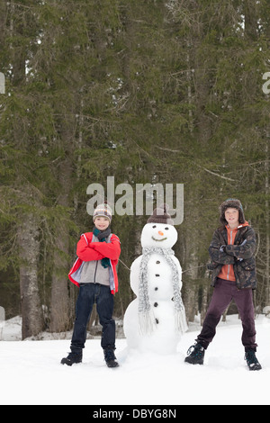 Porträt von zuversichtlich jungen neben Schneemann im Wald Stockfoto