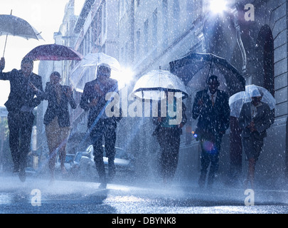 Geschäftsleute mit Sonnenschirmen im Regen laufen Stockfoto