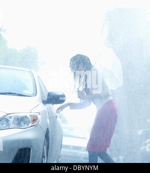Frau mit Regenschirm für Auto Türgriff im Regen zu erreichen Stockfoto