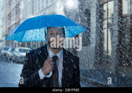 Porträt der Geschäftsmann mit winzigen Schirm im Regen Stockfoto