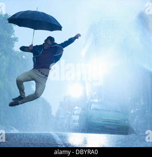 Begeisterten Mann mit Schirm im Regen springen Stockfoto