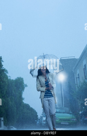 Glückliche Frau mit Regenschirm Wandern in Regen Stockfoto