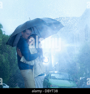 Glückliches Paar umarmt unter Dach im Regen Stockfoto