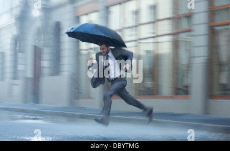 Geschäftsmann mit Regenschirm quer durch verregnete Straße Stockfoto