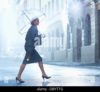 Glücklich Geschäftsfrau mit Regenschirm zu Fuß über die verregnete Straße Stockfoto