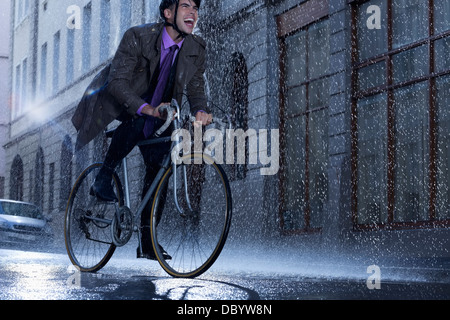 Begeisterte Unternehmer Reiten Fahrrad im verregneten Straße Stockfoto