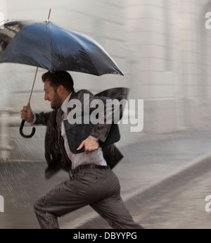 Geschäftsmann mit Schirm im Regen laufen Stockfoto