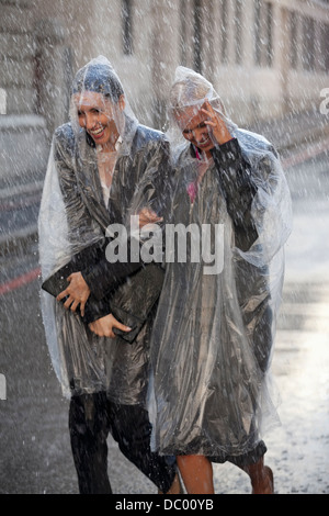 Unternehmerinnen in Ponchos auf verregnete Straße Stockfoto