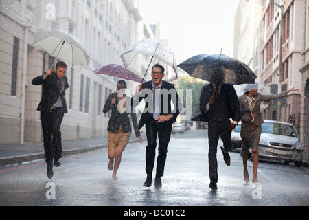 Geschäftsleute mit Sonnenschirmen im verregneten Straße laufen Stockfoto