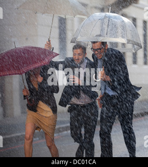 Glücklich Geschäftsleute mit Sonnenschirmen im verregneten Straße laufen Stockfoto