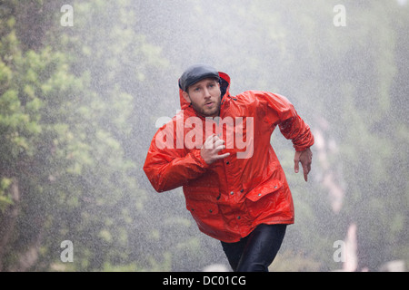 Mann im Regenmantel laufen im Regen Stockfoto