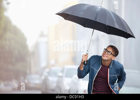 Mann mit Schirm nach oben auf Regen in der Straße Stockfoto