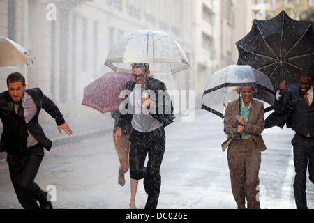 Begeisterte Geschäftsleute mit Sonnenschirmen im verregneten Straße laufen Stockfoto