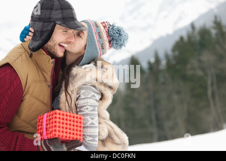Brautpaar mit Weihnachten Geschenk kissing in schneebedecktes Feld Stockfoto