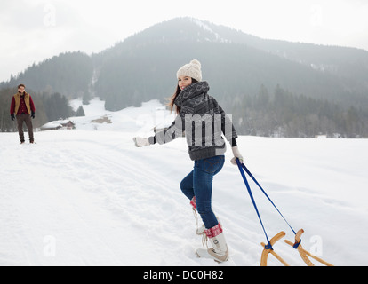 Porträt der lächelnde Frau zieht Schlitten in schneebedecktes Feld Stockfoto