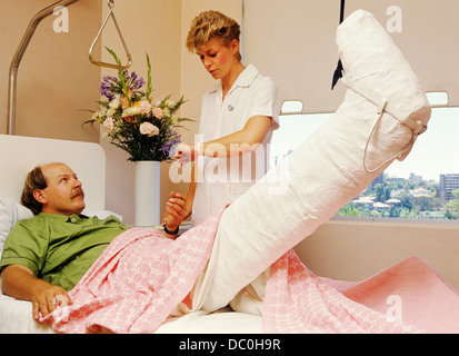 1980ER 1990ER MANN KRANKENHAUS BETT GEBROCHENES BEIN IN FORM UND ZUG WEIBLICHE SCHWESTER NIMMT SEINEN PULS VITALWERTE Stockfoto