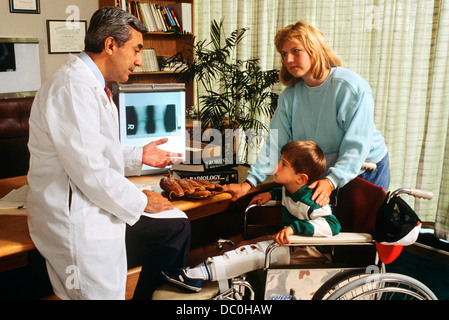 1990ER JAHREN ARZT ERKLÄREN, DIAGNOSE, KLEINER JUNGE IM ROLLSTUHL UND SEINE MUTTER Stockfoto