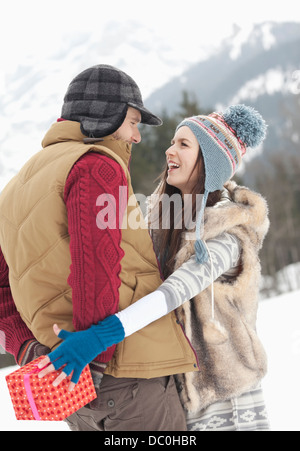 Frau für Weihnachtsgeschenk hinter Mann zurück in schneebedeckten Feld erreichen Stockfoto