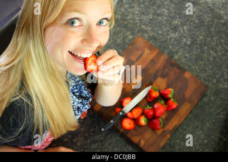 Eine attraktive Frau, die Verkostung einer Erdbeere während des Schneidens, gesundes Obst Stockfoto