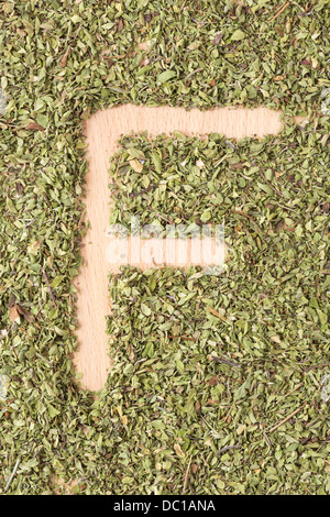 Buchstabe F geschrieben mit Oregano auf Holztisch Stockfoto