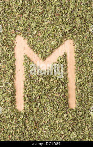 Buchstabe M geschrieben mit Oregano auf Holztisch Stockfoto