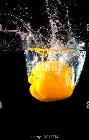 Frische gelbe Paprika planschen im Wasser auf schwarzem Hintergrund Stockfoto