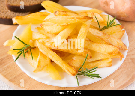 Portion hausgemachte Pommes Frites (Kartoffeln) mit Rosmarin auf weißen Teller und Holzbrett horizontal, Nahaufnahme Stockfoto