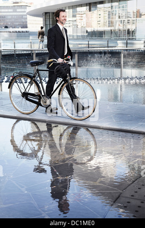 Mitte adult Geschäftsmann zu Fuß mit dem Fahrrad durch Wasserspiel in Stadt Stockfoto