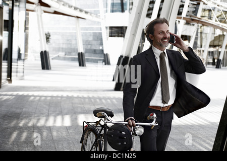 Mitte adult Geschäftsmann zu Fuß mit dem Fahrrad und mit Handy Stockfoto