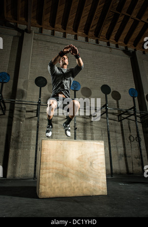 Junger Mann springt aus Holzkiste im Fitness-Studio Stockfoto