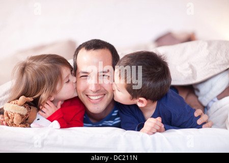 Sohn und Tochter küssen Väter Wange unter Bettdecke Stockfoto