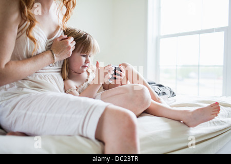 Frau und Mädchen sitzen auf Bett, Blick auf smartphone Stockfoto