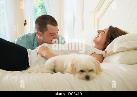 Schwangere Frau und Partner auf Bett liegend mit Hund Stockfoto