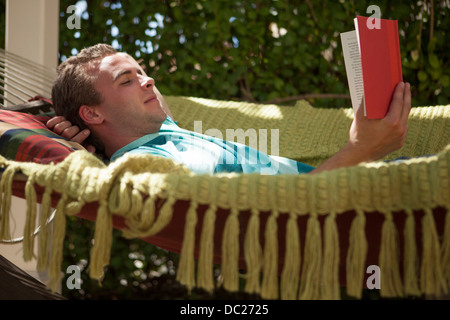 Junger Mann Lesebuch in Hängematte Stockfoto