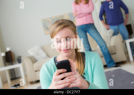 Teenager-Mädchen mit Handy, Eltern im Hintergrund Stockfoto