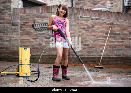 Eine Mädchen im Alter von 10 verwendet einen Hochdruckreiniger zur Reinigung des Block ebnen Antrieb auf ihre Familie zu Hause für Taschengeld. Stockfoto