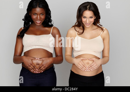 Zwei schwangere Frauen machen Herzformen mit Händen auf Bauch Stockfoto
