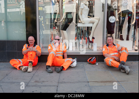 Drei Arbeiter in orange Hi Vis Kleidung machen Sie eine Pause vor einem Geschäft in London UK Stockfoto