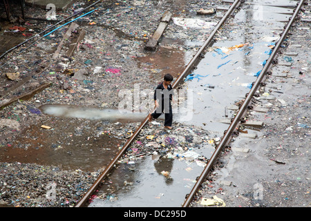 Junge geht durch Pfützen und Schmutz der Bandra Slumgebiet mit Schienen durch Stockfoto