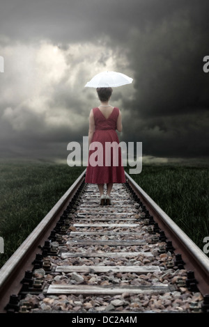 eine Mädchen in einem roten Kleid mit einem Sonnenschirm steht auf Bahngleise Stockfoto