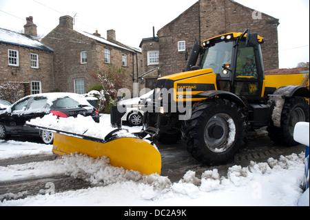 Ein Traktor mit einer Körnung Verbreitung Maschine ausgestattet Antriebe durch eine kleine verschneite Straße in Askrigg, North Yorkshire Stockfoto