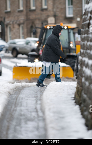 Ein Traktor mit einer Körnung Verbreitung Maschine ausgestattet Antriebe durch eine kleine verschneite Straße in Askrigg, North Yorkshire Stockfoto